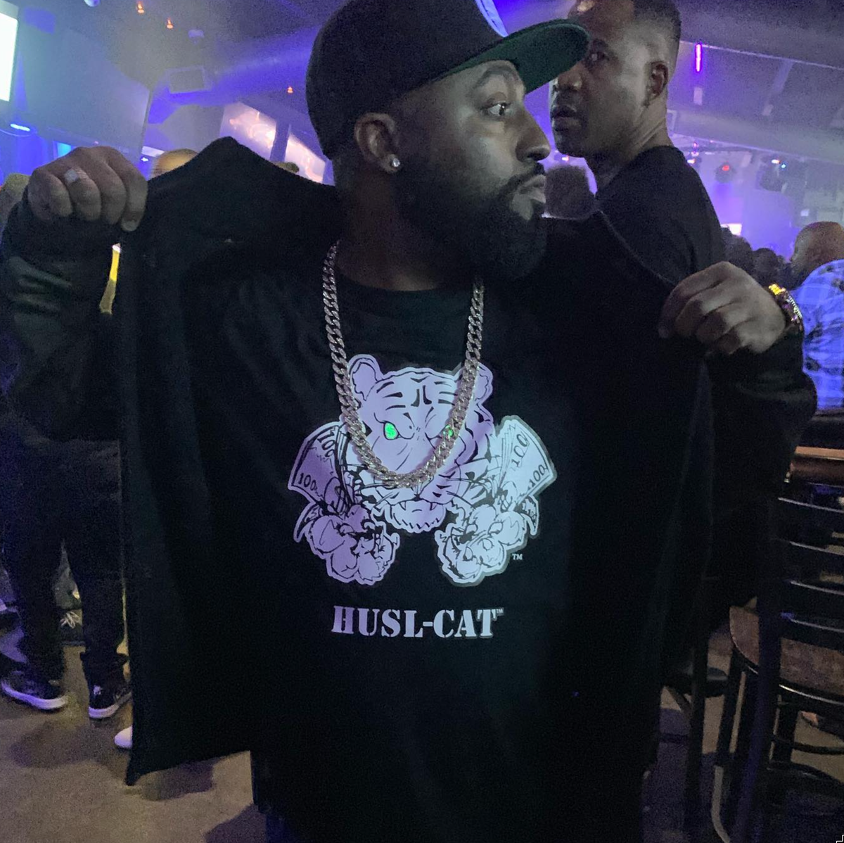 Man wearing a black HUSL-CAT T-shirt with a purple tiger graphic at an event